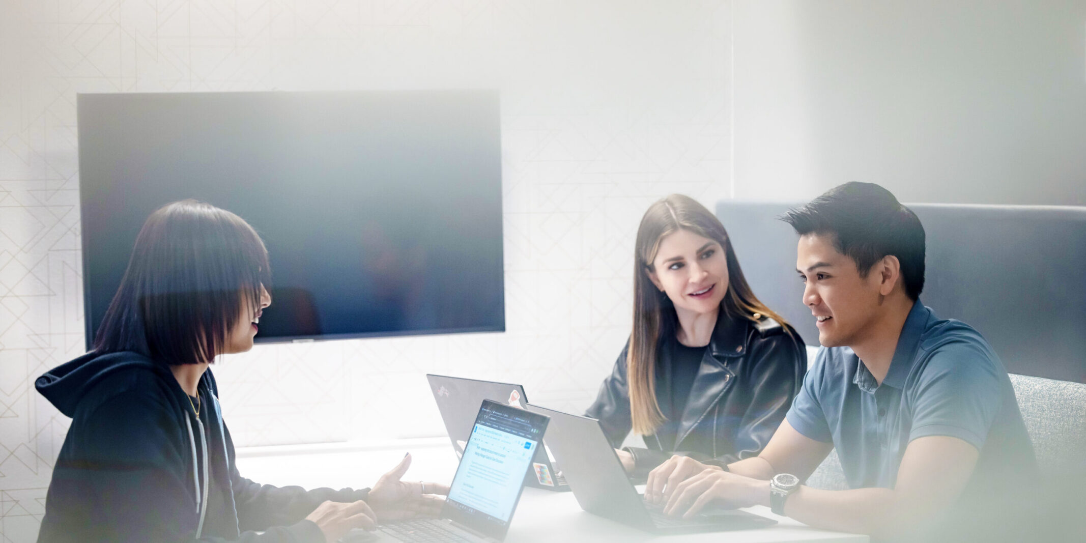 Three Two Sigma engineers collaborate at a table with their laptops.